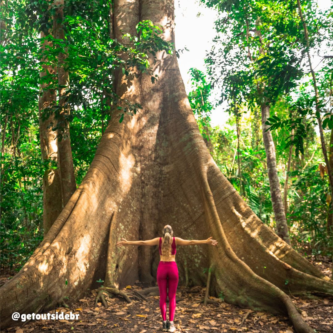 Mulher de braços abertos em frente a uma árvore Samaúma, em Alter do Chão